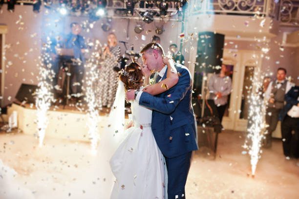 Newly married couple dancing on their wedding party with heavy smoke, multicolored lights and fireworks on the background.
